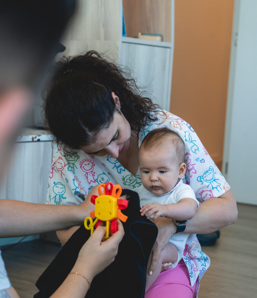 A fisioterapeuta Luísa realiza uma sessão de osteopatia pediátrica, interagindo de forma delicada com um bebé deitado na marquesa